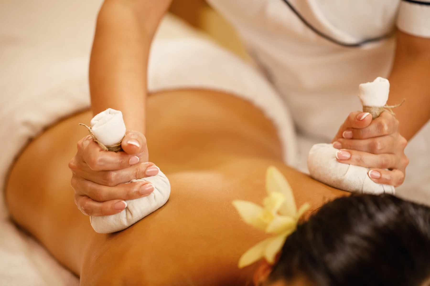 Foto ilustrativa de massagem com pindas, com fundo claro e ambiente simples